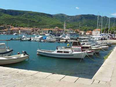 Petits bateaux amarrés dans le port de Hvar, avec les collines verdoyantes et le clocher de la ville en 
												arrière-plan, en Croatie