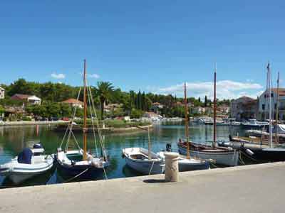 Bateaux traditionnels amarrés dans un petit port paisible de Hvar, entouré de maisons en pierre, de palmiers 
												et de cyprès (road trip Croatie