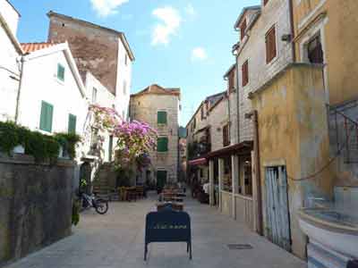 Ruelle pittoresque de Hvar en Croatie avec des maisons en pierre, des volets verts, une terrasse de café 
												et un bougainvillier en fleurs