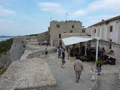 Touristes visitant la forteresse de Hvar, avec ses remparts en pierre, un café en terrasse et 
												une vue panoramique sur la mer Adriatique (road trip en Croatie)
