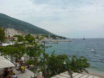 Vue sur le port de Bol sur l'île de Brač lors d'un roasd trip en Croatie, avec ses terrasses de cafés, ses bateaux 
												et les collines en arrière-plan