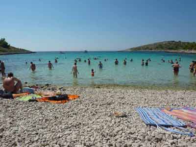 Plage de galets en Croatie avec de nombreux baigneurs dans une eau turquoise, sous un ciel bleu éclatant