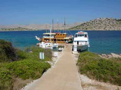 Petit quai dans le parc national des Kornati (road trip en Croatie), avec plusieurs bateaux amarrés sur une 
												mer turquoise entourée de collines arides