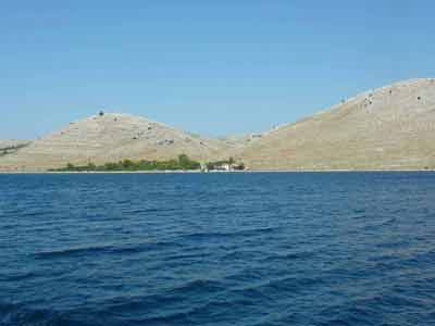 Colline aride du parc national des Kornati en Croatie, vue depuis la mer Adriatique avec une bâtisse isolée en 
												contrebas