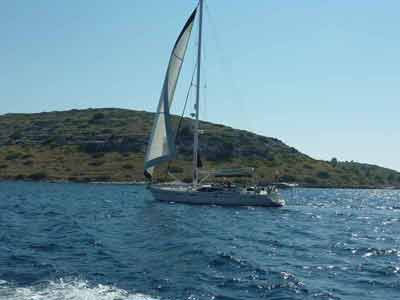 Voilier naviguant sur les eaux bleues du parc national des Kornati en Croatie, avec une île aride en arrière-plan