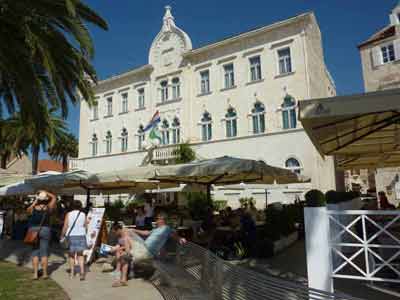 Façade blanche ornée de l'hôtel de ville de Trogir avec terrasses et promeneurs