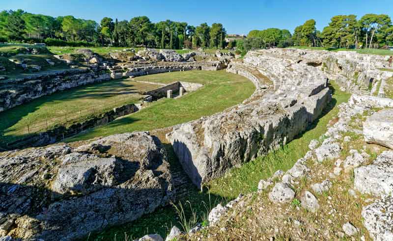 Amphithéâtre romain de Syracuse en Sicile, vestiges archéologiques majestueux entourés de verdure, ciel bleu lumineux et héritage historique fascinant