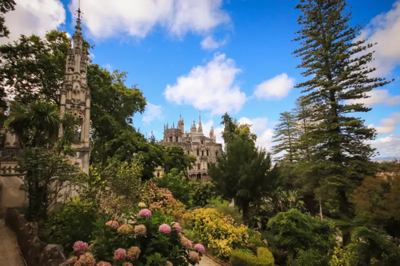 Jardins luxuriants de la Quinta da Regaleira à Sintra avec vue sur le palais gothique au loin sous un ciel bleu