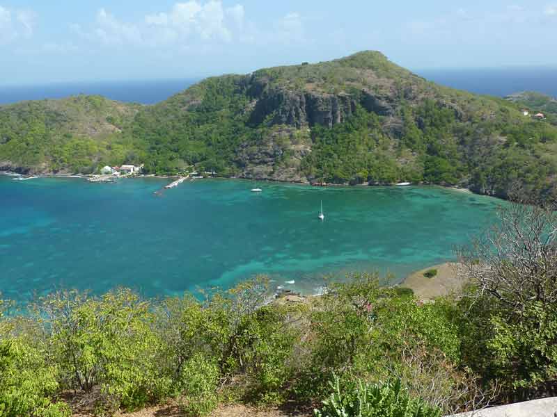 Vue imprenable depuis le fort Napoléon aux Saintes en Guadeloupe, dévoilant une baie aux eaux turquoise, entourée de collines verdoyantes, avec des voiliers ancrés dans le calme de la mer des Caraïbes
