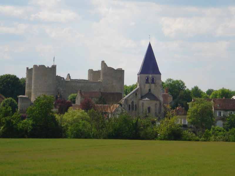 Vue du village de Yèvre-le-Châtel avec les ruines imposantes de son château médiéval et son église en pierre, entourés de 
								verdure sous un ciel partiellement nuageux