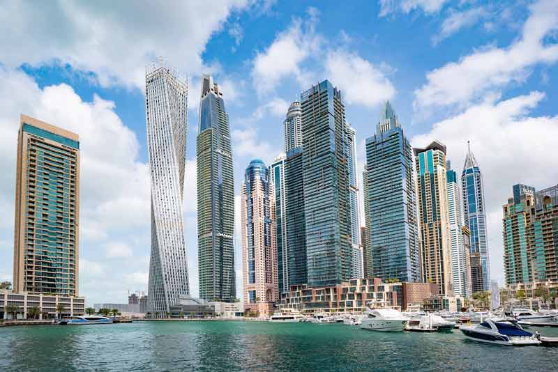 Vue sur la marina de Dubaï avec une skyline de gratte-ciel modernes bordant l’eau turquoise et des yachts amarrés au premier plan