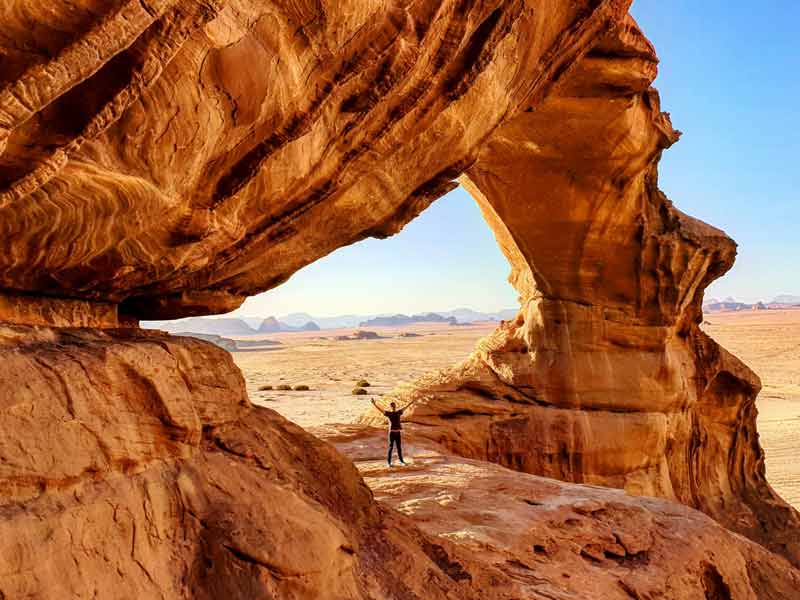 Pont rocheux naturel dans le désert du Wadi Rum, Jordanie, avec un voyageur admirant l’arche sculptée par l’érosion