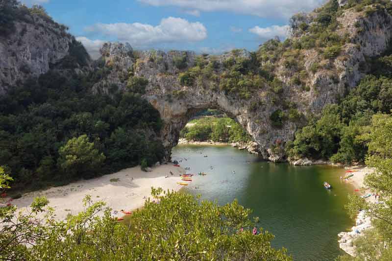 Vue sur le pont d'Arc en Ardèche, arche naturelle spectaculaire au-dessus de la rivière, avec des canoës et une plage en été