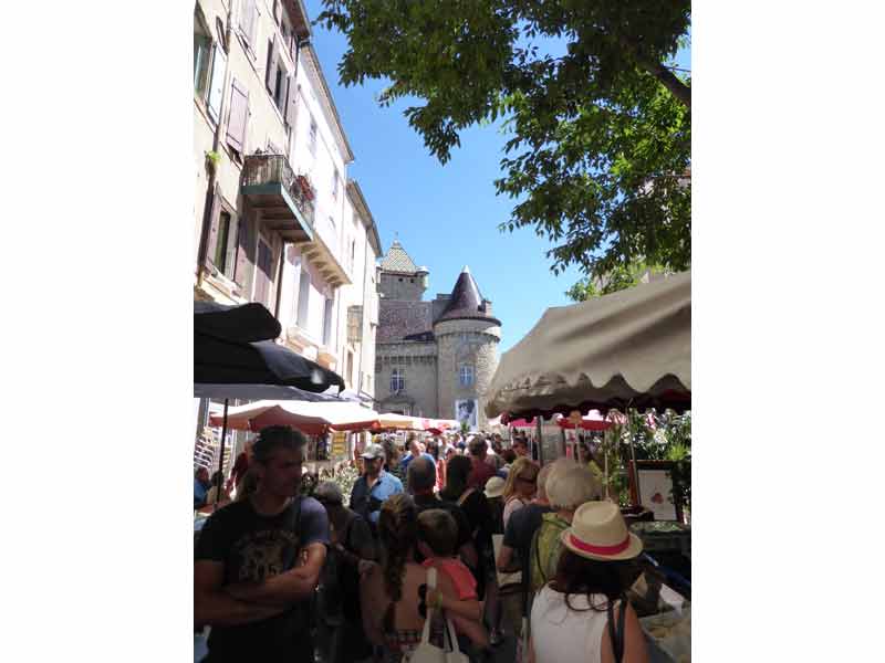 Marché animé à Aubenas en Ardèche, avec foule de visiteurs, étals de produits locaux et vue sur le château médiéval