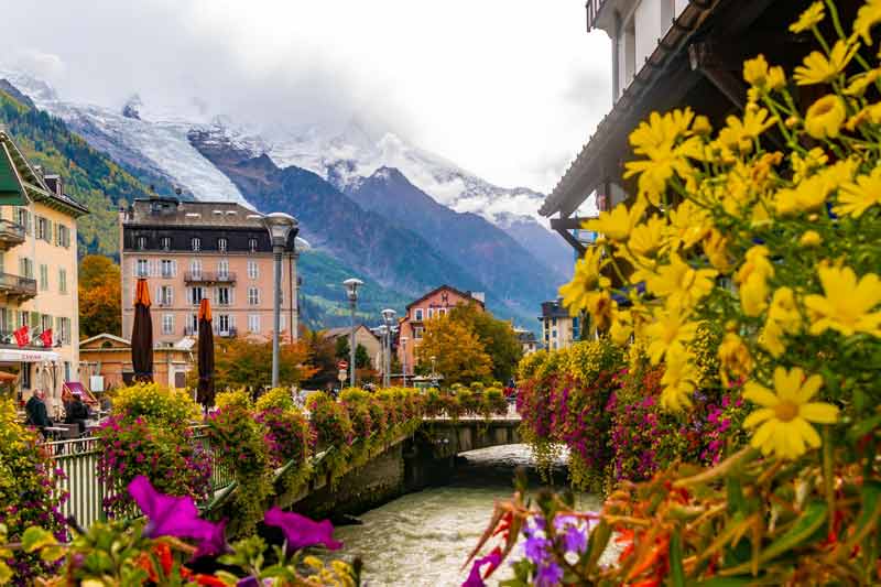 Vue colorée de Chamonix avec ses maisons alpines, le torrent qui traverse la ville et les montagnes enneigées du massif du Mont-Blanc en arrière-plan