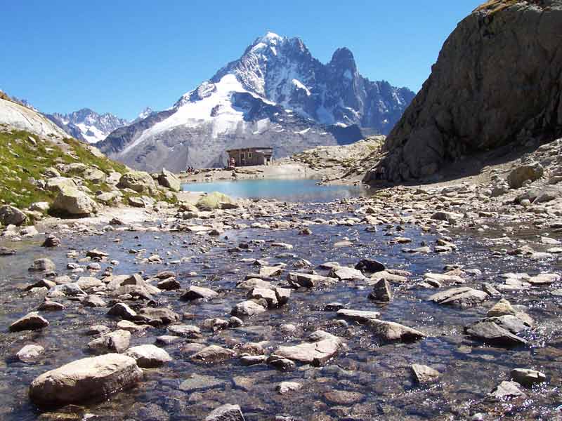 Ruisseau alpin et roches en premier plan avec vue sur le lac Blanc et les sommets du massif du Mont-Blanc