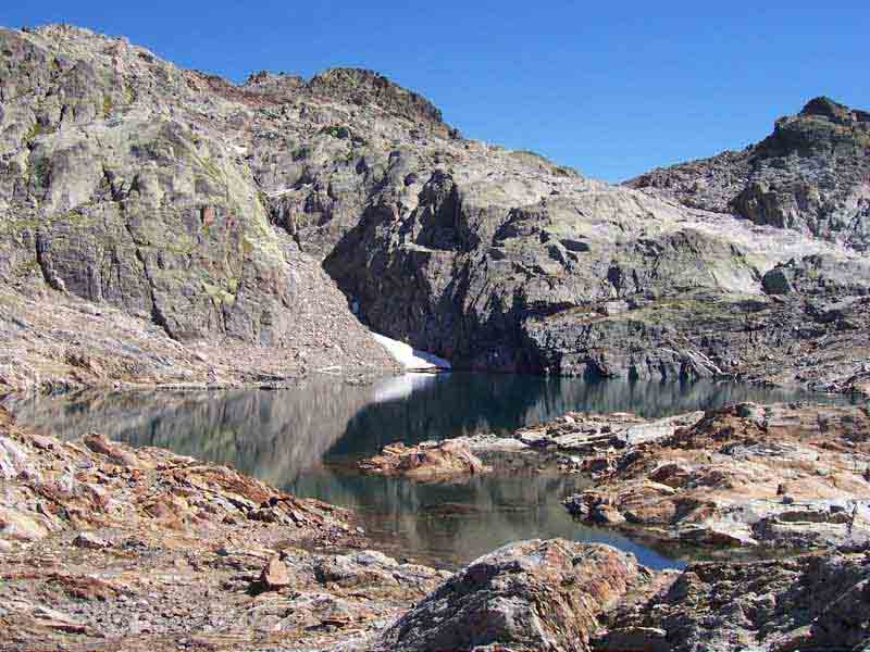 Lac Cornu niché dans un cirque rocheux, avec eaux sombres contrastant avec les parois claires des Aiguilles Rouges
