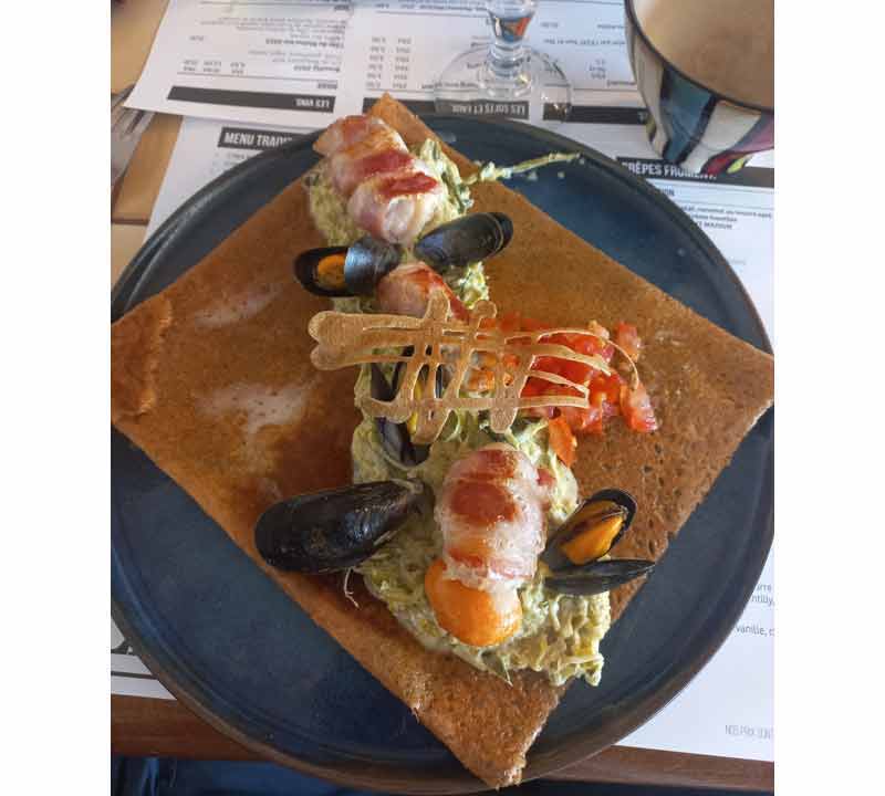 Galette de sarrasin garnie de noix de Saint-Jacques au lard, de moules et de tomates, servie dans une crêperie du pays Fouesnantais