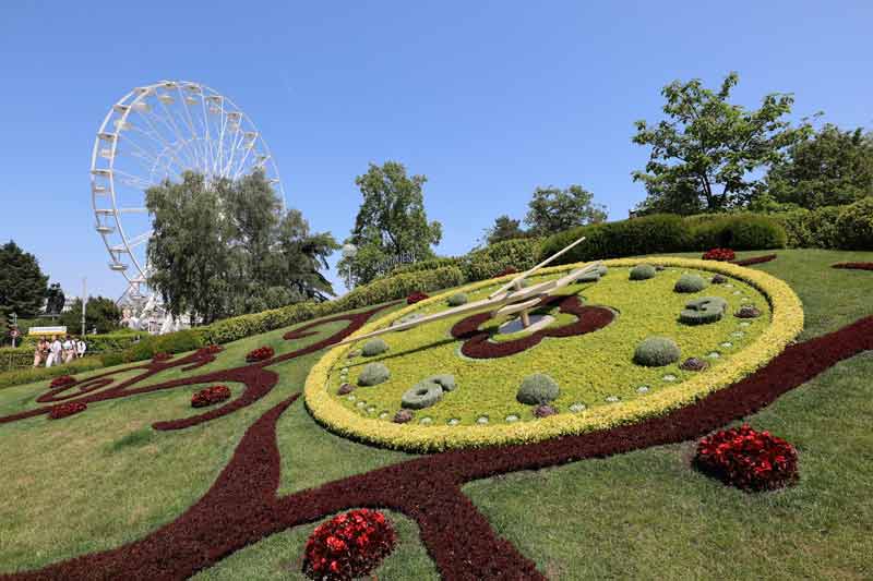 Horloge fleurie de Genève dans le Jardin anglais avec grande roue en arrière-plan, un classique à découvrir quand on vient visiter Genève