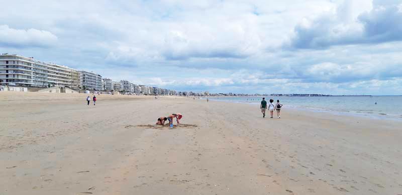 Promeneurs et enfants jouant sur la grande plage de La Baule, bordée d'immeubles modernes sous un ciel nuageux