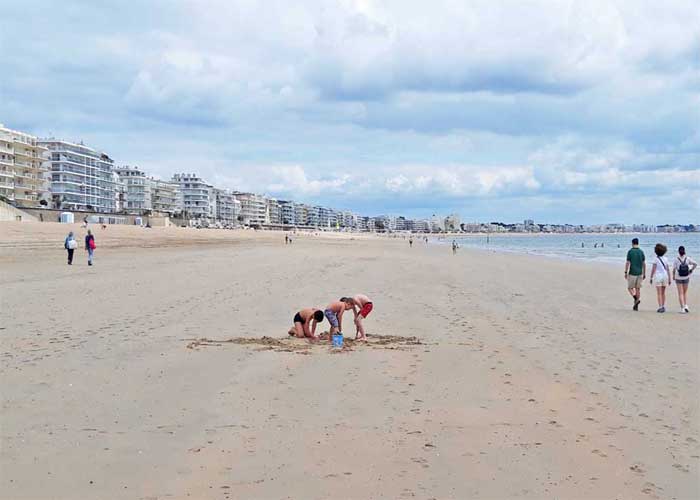 Promeneurs et enfants jouant sur la grande plage de La Baule, bordée d'immeubles modernes sous un ciel nuageux