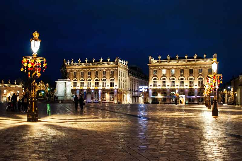 Place Stanislas de Nancy illuminée la nuit avec ses bâtiments et réverbères dorés