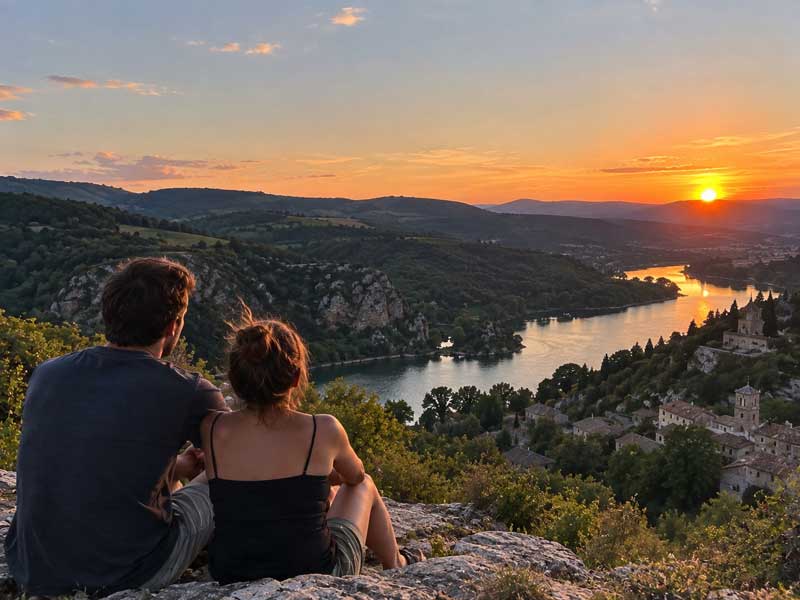 Couple assis sur un rocher face au coucher de soleil sur les gorges de la Loire, pour un week-end romantique dans la Loire