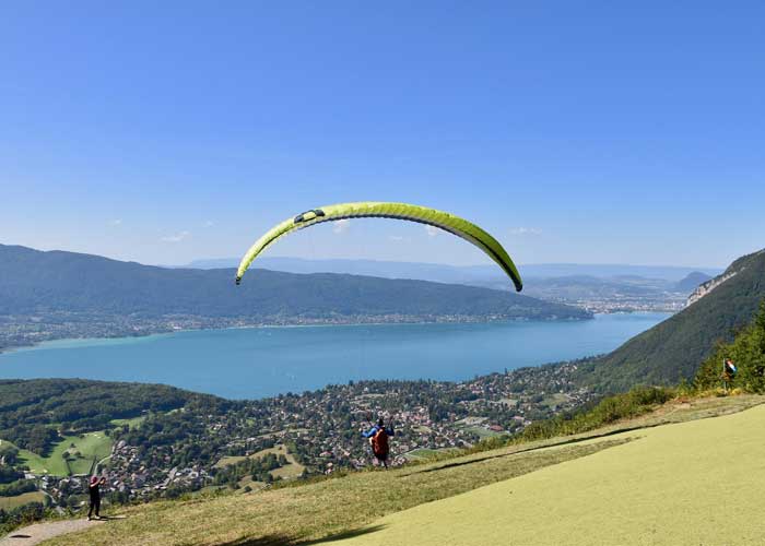 Parapentiste gonflant sa voile verte sur l’aire de décollage du col de la Forclaz, avec vue plongeante sur le lac d’Annecy