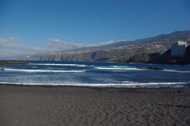 Plage de sable noir de Playa de la Arena à Tenerife, bordée par les vagues de l’Atlantique et les reliefs volcaniques de la côte