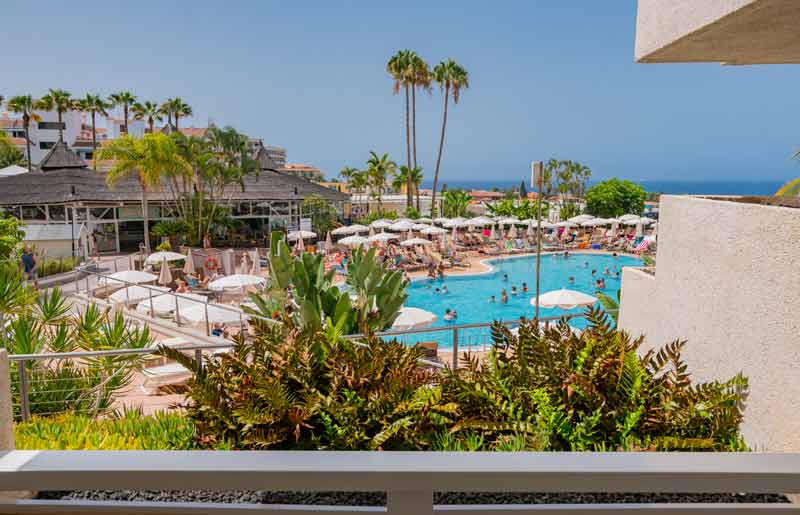 Piscine du Landmar Playa La Arena à Tenerife entourée de palmiers et de transats, avec vue sur l’océan Atlantique en arrière-plan