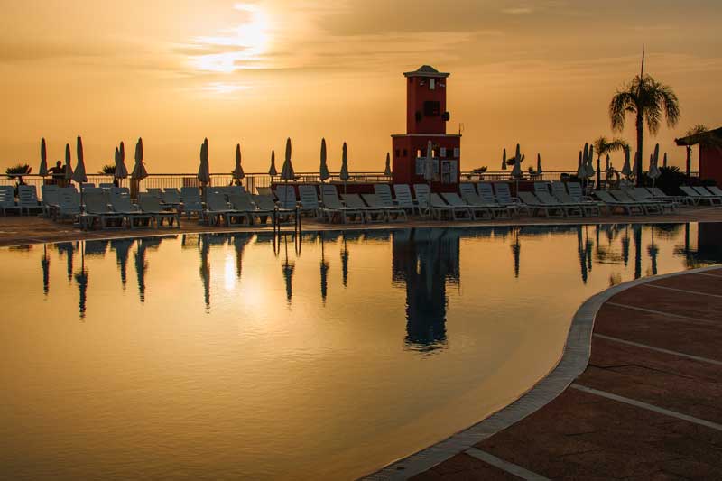 Coucher de soleil sur la piscine du Landmar Costa Los Gigantes à Tenerife, avec ses transats et sa tour qui se reflètent dans l’eau
