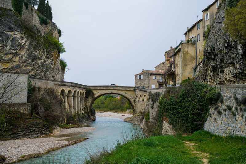 Pont romain de Vaison-la-Romaine enjambant la rivière, entouré de falaises et de maisons en pierre typiques du Vaucluse