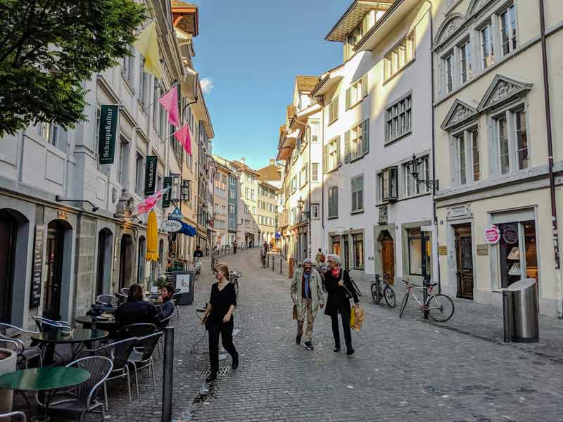 Rue animée du quartier Niederdorf à Zurich avec terrasses de cafés et maisons traditionnelles